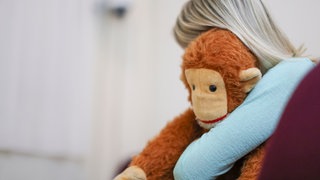 ILLUSTRATION: Eine junge Frau sitzt mit einem Kuscheltier im Arm in einem Raum des Childhood House, in dem Kinder und Jugendliche, die von Missbrauchs betroffen sind, betreut werden (gestellte Szene).