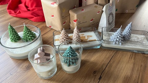 Kerzen in der Form von Tannenbäumen oder Lebkuchen-Männchen sind in alten, abgebrannten Duftkerzengläsern neu arrangiert, hier auch mit Glitzerstaub.