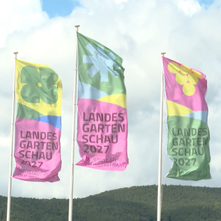 Landesgartenschau-Fahnen im Wind, dahinter bewaldete Berge