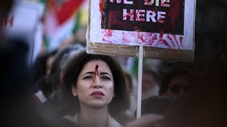 Eine Teilnehmerin mit einem roten blutähnlichen Fleck auf der Stirn hält ein Plakat bei einer Kundgebung zur Unterstützung der Demonstranten im Iran.