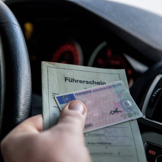 Person hält im Auto seinen Führerschein in der Hand