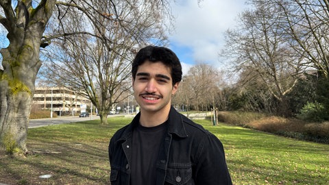 Halil steht in einem Park. Der 16-jährige macht eine Ausbildung zum Kaufmann für Büromanagement.