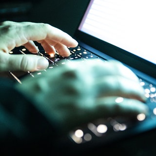 Eine Person tippt mit den Fingern auf einer beleuchteten Laptop-Tastatur (gestellte Szene). Die Staatsanwaltschaft Landau und die Kriminalpolizei ermitteln gegen einen Schulleiter aus der Vorderpfalz. Es geht um Kinderpornografie.