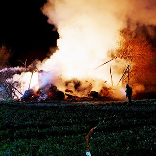 Ein Feuerwehrmann löscht bei Speyer die lichterloh brennenden Überreste einer Scheune