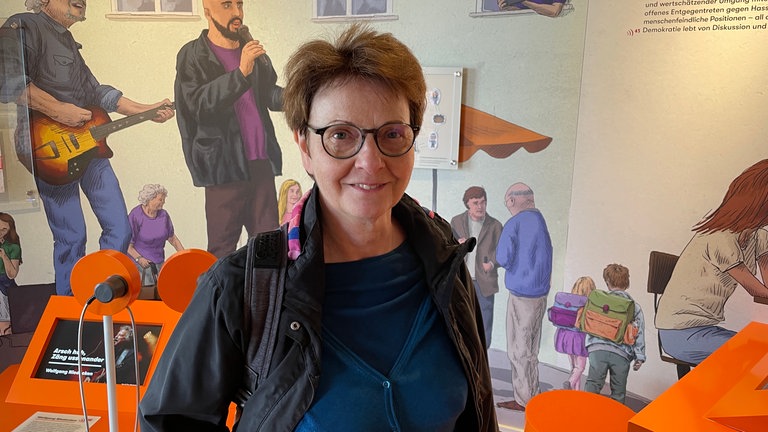 Besucherin Eva Loleit steht in einem Raum, in der es eine Ausstellung gibt. Sie hatte es, wie sie sagt, nicht weit zum Hambacher Schloss und fand es wichtig, am Tag der Demokratiegeschichte zu kommen. Für sie ist Demokratie ein zentrales Thema. Außerdem hat sie sich wie viele andere auch sehr über den kostenfreien Eintritt gefreut.