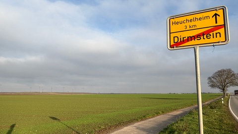 Ortsschild von Dirmstein (Kreis Bad Dürkheim: in der Ackerlandschaft nahe der Gemeinde dürfen 16 weitere Windräder gebaut werden. Einigen Anwohnern sind insgesamt 30 hohe Windkraftanlagen zu viel. Der Gemeinderat Dirmstein hat das Projekt der BayWa jedoch genehmigt.