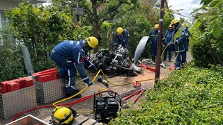 Einsatzkräfte schneiden den Motor des abgestürzten Kleinflugzeugs in zwei Teile, um ihn besser abtransportieren zu können.