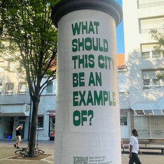 "What should this city be an example of?" steht groß auf einer Litfaßsäule in Ludwigshafen. Das Ganze ist eine Aktion des Ludwigshafener Kunstvereins.