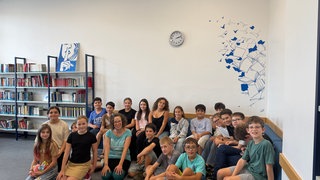 Schüler am Carl-Bosch-Gymnasium in Ludwigshafen und eine Lehrerin sitzen zusammen in einem Klassenzimmer.
