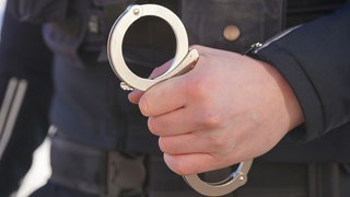Ein Polizist hält Handschellen in der Hand (Symbolbild). Insgesamt drei Drogendealer sind von der Polizei in Ludwigshafen festgenommen worden. Die Polizei fand 27 Kilogramm Drogen.
