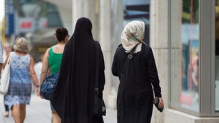 zwei muslimische Frauen in langen Gewändern und Kopftuch in Fußgängerzone, Symbol für "Wie hat sich das Leben von Muslimen seit den Terroranschlägen 2001 verändert?"