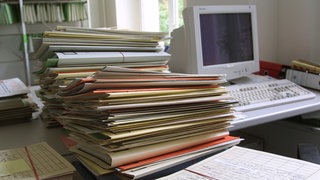 Auf dem Schreibtisch des Büros stapeln sich die Akten und warten darauf, bearbeitet zu werden.
