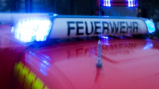Ein Feuerwehrauto steht mit blinkendem Blaulicht auf der Straße.