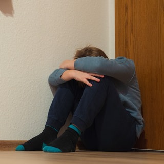 Ein Junge kauert sich in der Ecke seines Zimmers am Fußboden sitzend zusammen. Bei dem Foto handelt es sich um ein Sujetbild.