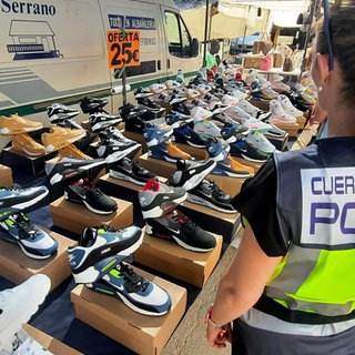 Eine spanische Polizistin steht vor einem Verkaufsstand mit gefälschten Markensportschuhen. 