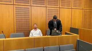 Der Angeklagte sitzt auf der Anklagebank, neben ihm steht sein Verteidiger.
