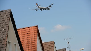 Ein Flugzeug überfliegt Häuser (Symbolbild). Durch ein neues Anflugverfahren soll Mainz vom Fluglärm entlastet werden. 