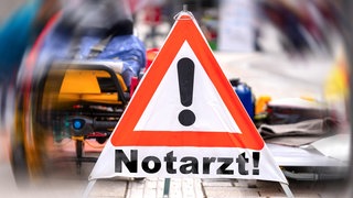 Notarzt-Warndreieick vor verschwommener Unfallstelle