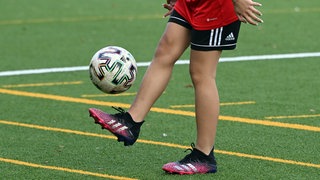 Ein Mädchen jongliert einen Ball auf einem Fußballplatz.