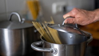 Eine Hand hebt den Deckel eines Nudeltopfs.