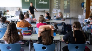 Schulkinder sitzen in einem Klassenraum und schauen auf die Tafel.
