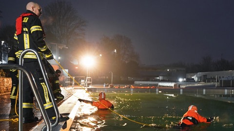 Zwei Feuerwehrleute hängen an Leinen im eiskalten Wasser des Wartbergbades in Alzey.