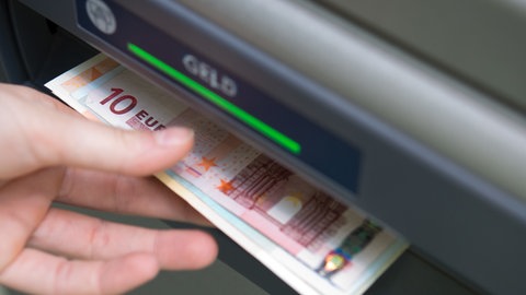 Eine Hand nimmt Geldscheine aus einem Geldautomaten. In Mainz wollte ein 18-Jähriger hilfsbereit sein und wurde um 1.500 Euro betrogen