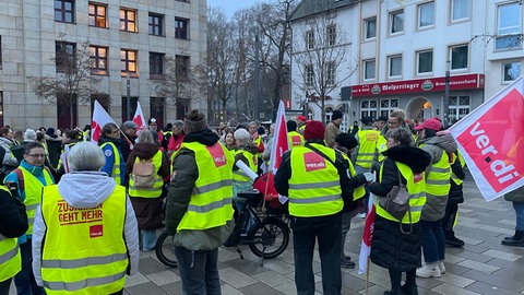 Rund 50 Streikende stehen in gelben Warnwesten und mit Fahnen der Gewerkschaft ver.di auf dem Kornmarkt in Bad Kreuznach.