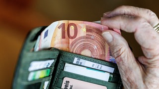Ene Hand nimmt Geldscheine aus einem Portemonnaie.