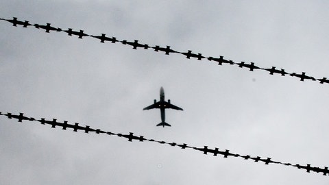 Ein Flugzeug am Himmel, durch Stacheldraht fotografiert. Ein aggressiver Flüchtling aus Windesheim im Kreis Bad Kreuznach soll mit so einem Flieger abgeschoben werden (Symbolbild)