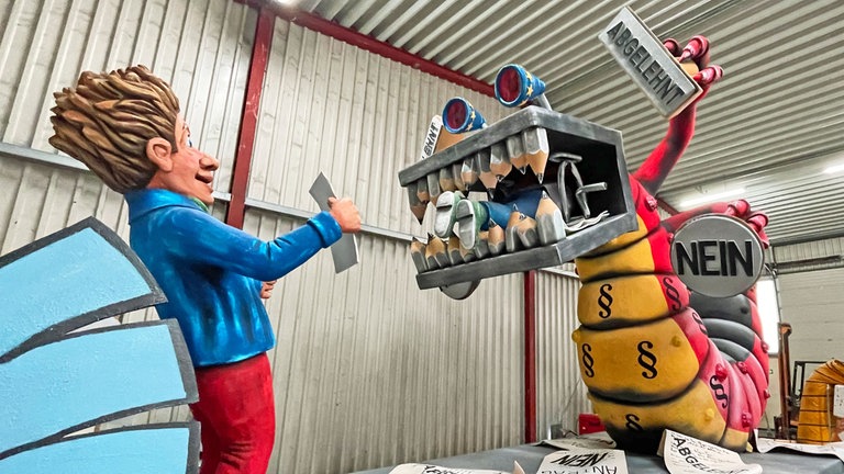 Der Wagen heißt "Bürokratiemonster". Das Monster frisst viel Papier, Personal und sagt gerne mal nein. Es wird als fett und nimmersatt beschrieben. 