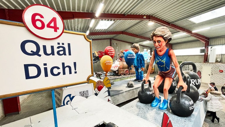 Der Wagen mit der Zugnummer 64 heißt "Quäl DIch!". Der text dazu lautet: Die EU in dieser Zeit braucht Wachstum und mehr Sicherheit! Wer schwach ist, wird besiegt von Lumpen – Europa muss Gewichte pumpen!