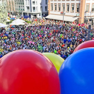 Am Balkon des Ostheimer Hofes sind bierfarbbunte Ballonsbefestigt. Unten feiern die Fastnachter. 
