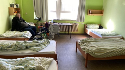 Ein Wohnsitzloser sitzt in einem Mehrbettzimmer.