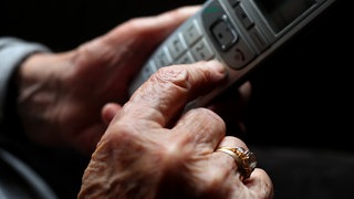 Eine ältere Frau hält ein Telefon in der Hand. In Mainz ist eine 85-Jährige per Telefonbetrug um Geld und Gold im Wert von 3.000 Euro gebracht worden