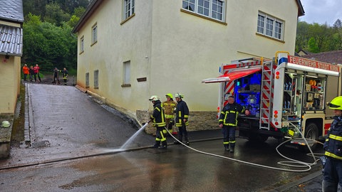 Feuerwehrleute reinigen nach einer Schlammlawine die Straße in Meckenbach.
