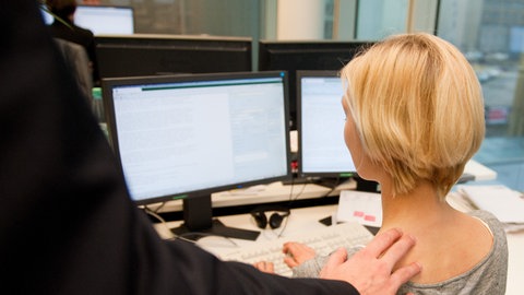 Ein Mann berührt in einem Büro die Schulter einer Arbeitskollegin (Symbolbild).