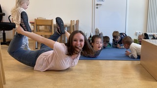 Lara liegt mit den Kindern der Kita bäuchlings auf dem Boden und hat sichtlich Spaß an ihren Spielen. Sie hat ihren Traumjob gefundden