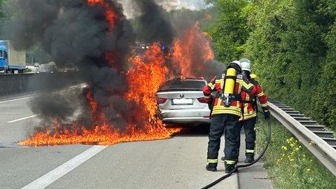 Feuerwehrleute löschen ein brennendes Auto, das auf dem Seitenstreifen der A61 bei Waldalgesheim steht. 