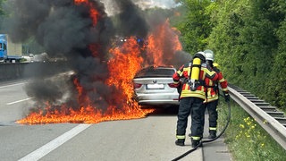 Feuerwehrleute löschen ein brennendes Auto, das auf dem Seitenstreifen der A61 bei Waldalgesheim steht. 