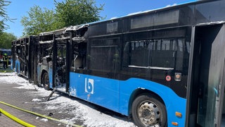 Vor dem ausgebrannten Gelenkbus liegen Löschschläuche. Unter dem Bus liegt Löschschaum.