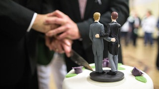 Zwei Bräutigam-Figuren stehen auf einer Hochzeitstorte.