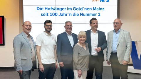 Beim MCV ist das Motto für die Fastnachtskampagne 2026 vorgestellt worden. MCV-Pressesprecher Michael Bonewitz, Hofsänger-Kapitän Vinzent Grimmel, MCV-Präsident Hannsgeorg Schönig, Fastnachtsikone und Ehrenbürgerin Margit Sponheimer, Oberbürgermeister Nino Haase und der Vorstandsvorsitzende der Volksbank Darmstadt-Mainz, Uwe Abel.