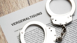 Handschellen liegen auf einem juritischem Papier: Das Landgericht Mainz hat einen Krankenpfleger verurteilt, der sein Kollegin vergewaltigt hatte. 
