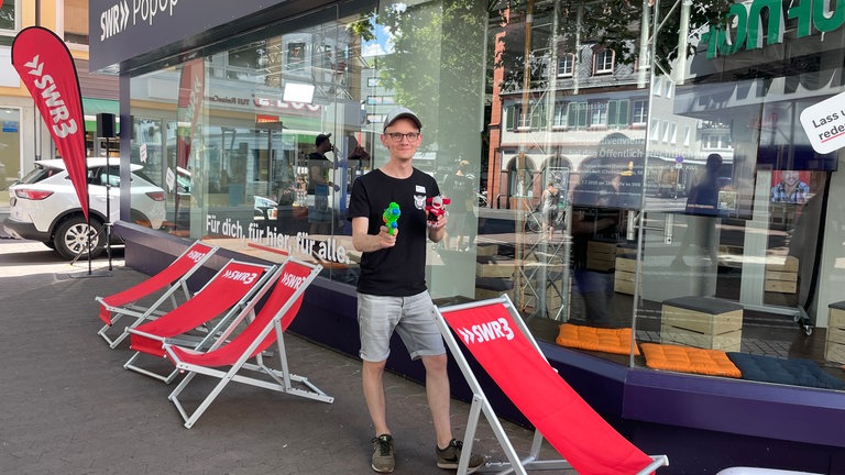SWR3-Reporter Jakob Reifenberg begrüßt Besucher des Pop-Up-Studios in Mainz mit einer Wasserpistole.