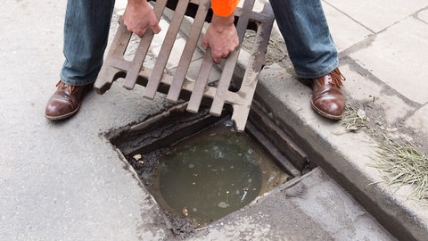 Ein Mann hebt einen Gullydeckel hoch. In Ingelheim sind mehr als 50 Gullydeckel geklaut worden. Jetzt gibt es einen Tatverdächtigen