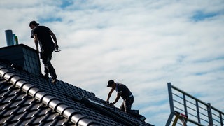 Zwei Männer arbeiten mit Werkzeug auf einem Hausdach.