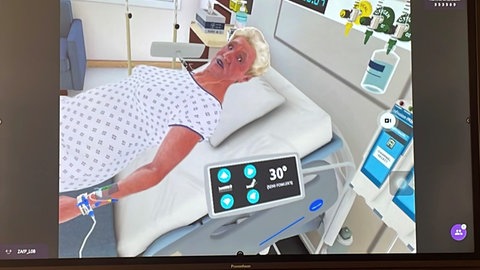 Ein Bildschrim zeigt eine virtuelle Patientin in einem virtuellen Krankenzimmer.