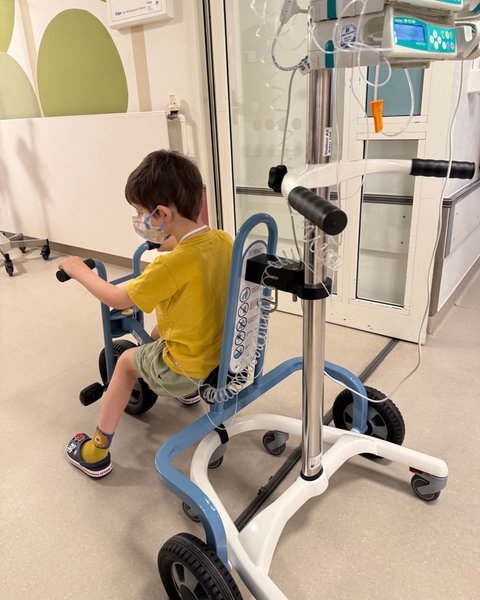 Ein Junge fährt mit einem speziellen Fahrrad über den Flur der Kinderkrebsstation in Mainz. An dem Rad kann ein Infusionsständer angebracht werden