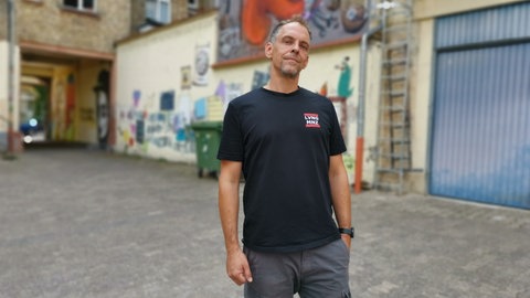 Dominik Mahr steht im Ollo-Hof in der Mainzer Neustadt. An den Wänden im Hintergrund sind Street-Art-Kunstwerke angebracht.
